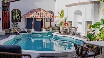 A swimming pool with a tiled deck, surrounded by plants and outdoor furniture.