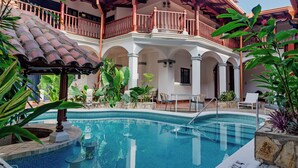 A pool area with a tiled deck, lounge chairs, and a covered balcony.
