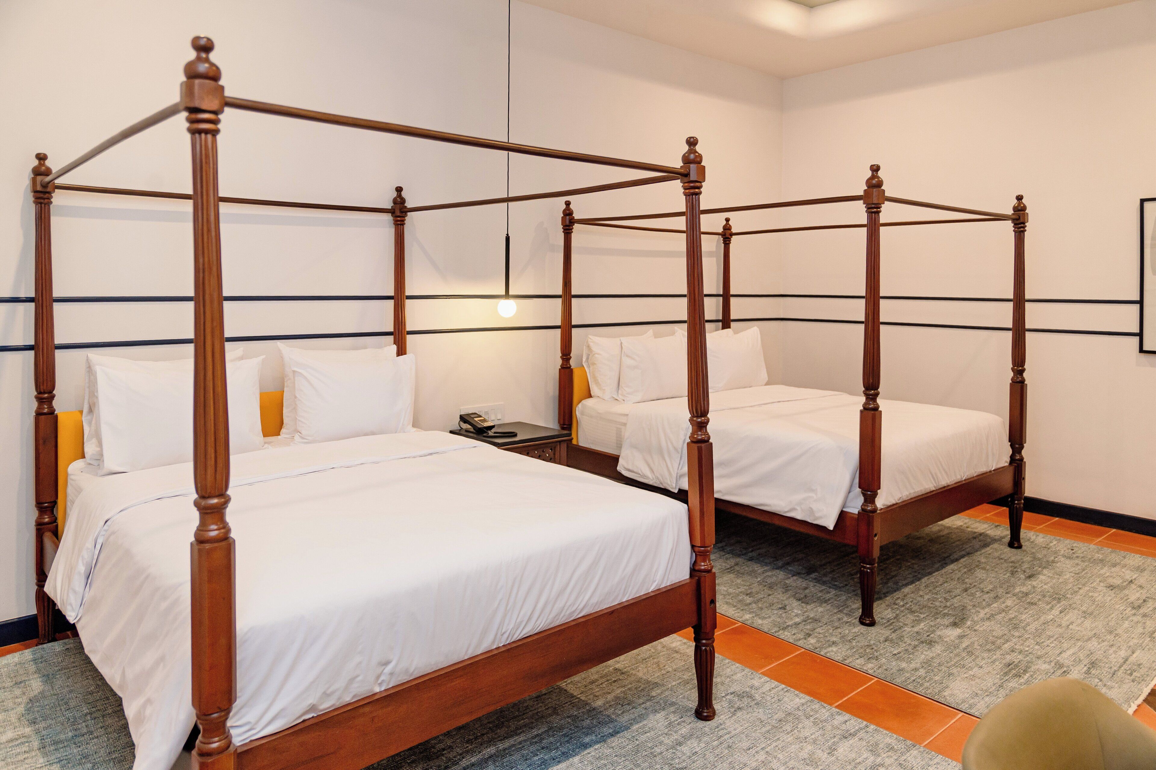 A hotel room with two four-poster beds, a small bedside table with a lamp, and a carpeted floor.