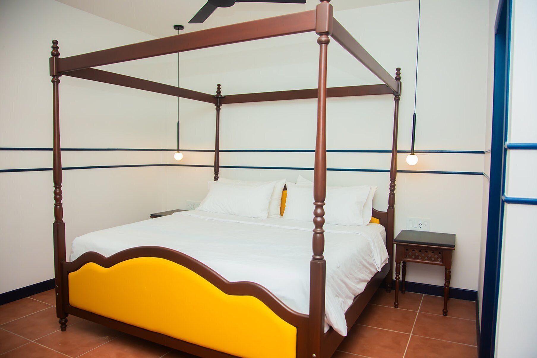 A four-poster bed with a yellow upholstered headboard in a hotel room with white walls and blue trim.