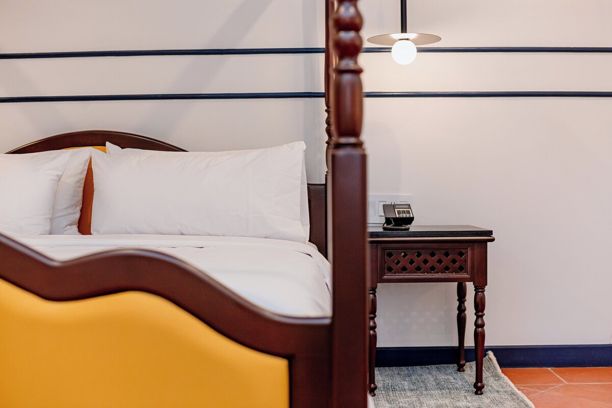 Een bed met witte lakens, een houten hoofdbord en een nachtkastje met een lamp en een telefoon.