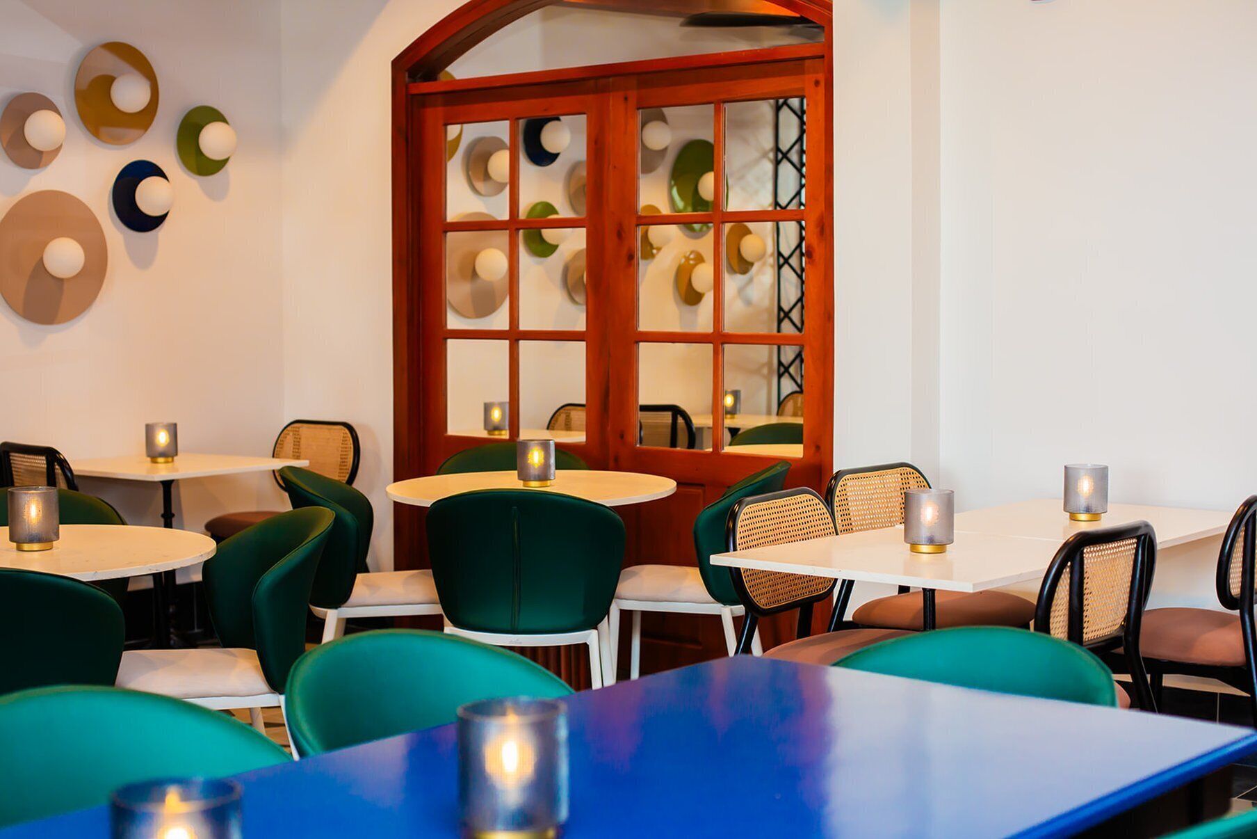 Ein Restaurantinneres mit runden Tischen und Stühlen, einer Holztür mit Glasfeldern und an der Wand befestigten Dekotellern.