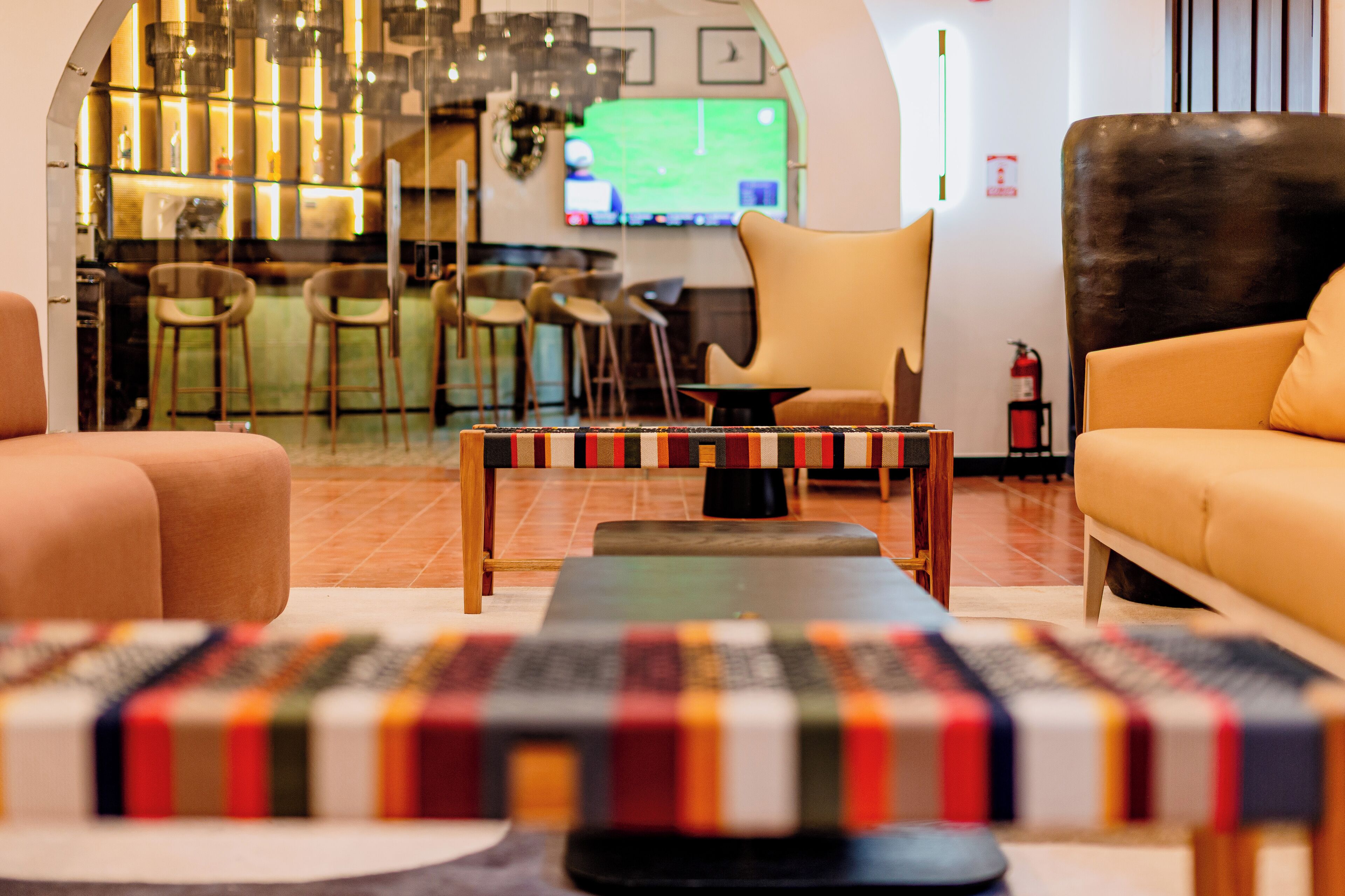 Et moderne loungeområde med en bar i baggrunden, behagelige siddepladser og et fjernsyn, der viser en sportsbegivenhed.