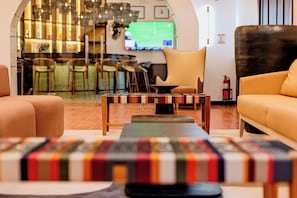 A modern lounge area with a bar in the background, comfortable seating, and a television displaying a sports game. - voco Lake Nicaragua Granada by IHG (Granada)