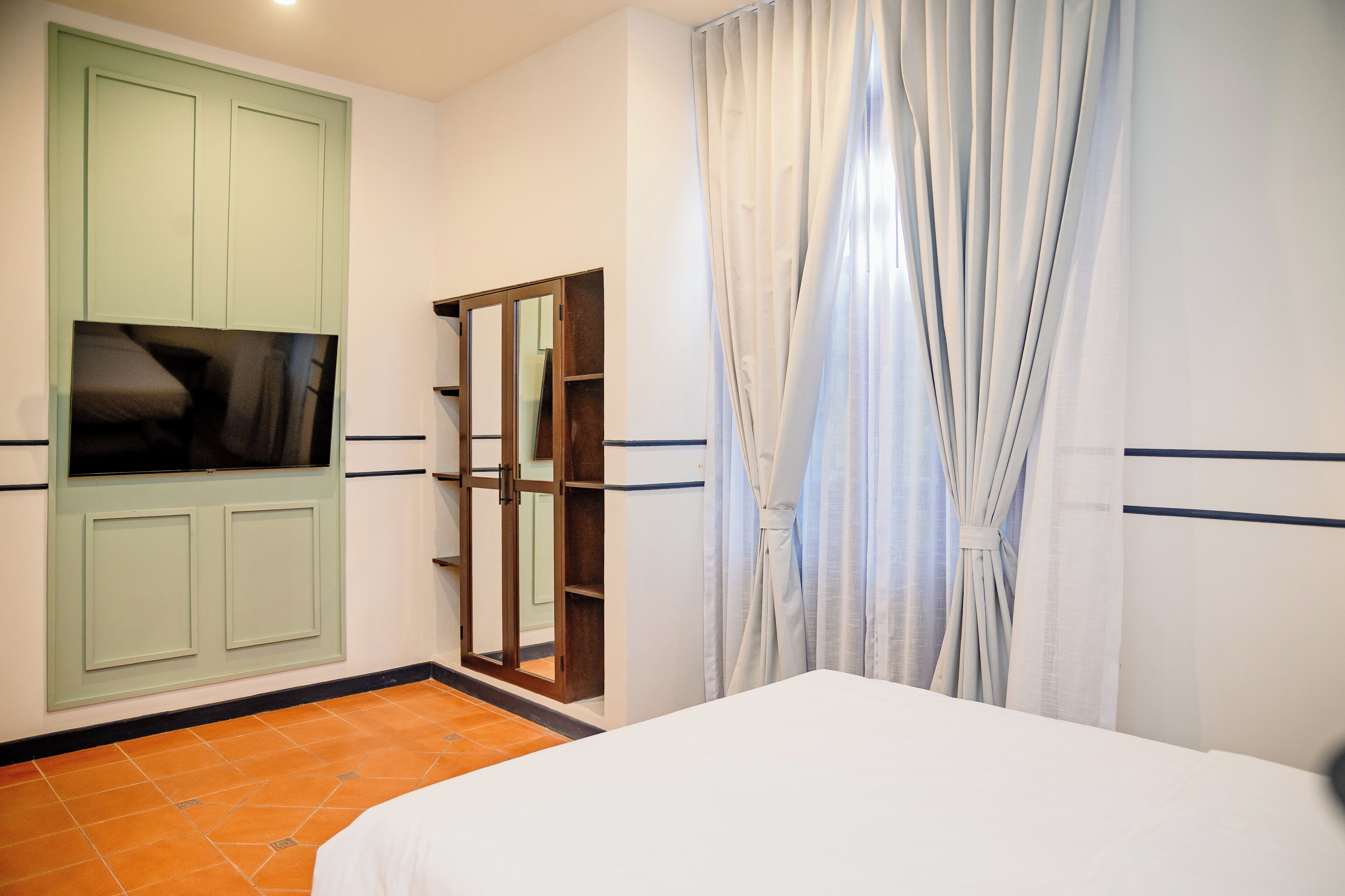 Een slaapkamer met een bed, een groene garderobe, een spiegel en een raam met gordijnen.