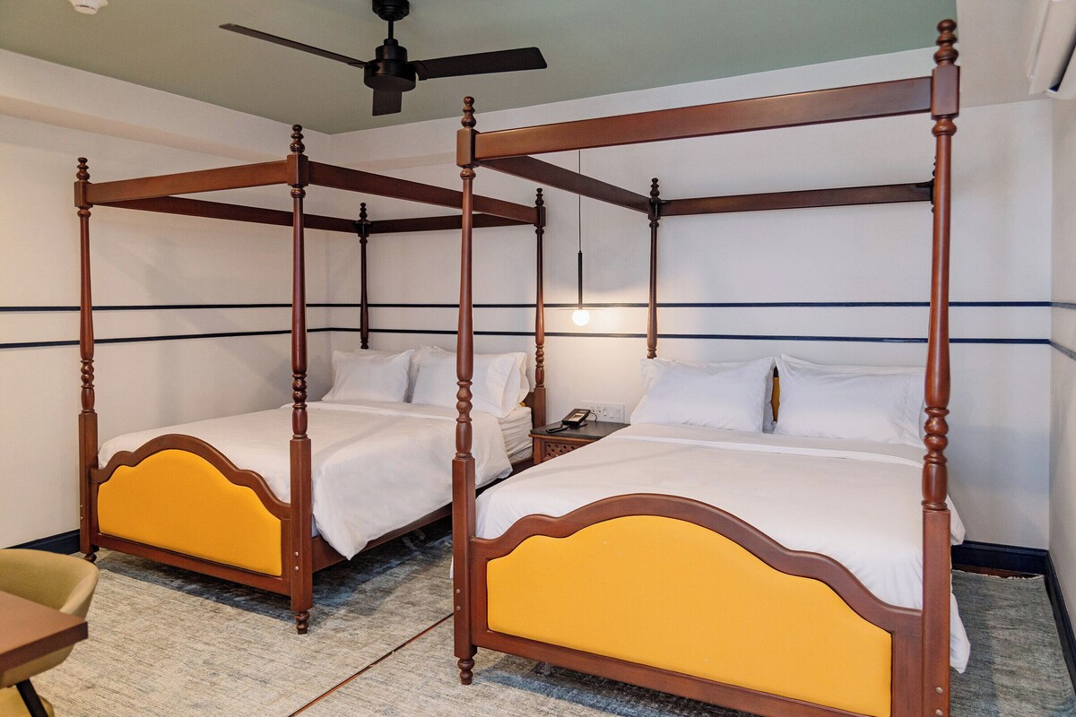 Een bed met hemelbed, met een geel bekleden hoofdbord, een nachtkastje en een bijzettafeltje met een telefoon.