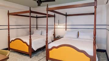 A four-poster bed with a yellow upholstered headboard, a bedside table, and a nightstand with a phone.