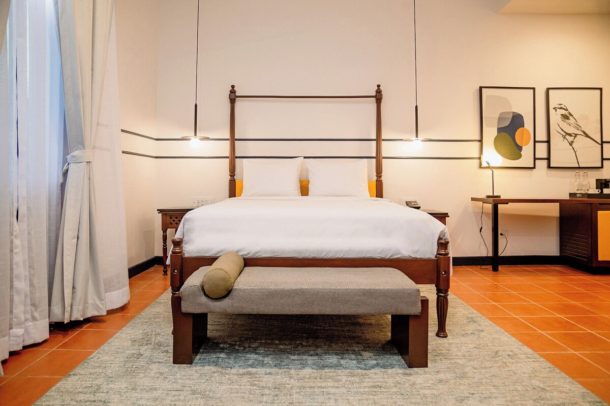 Een keurig opgeruimde slaapkamer met een hemelbed, een bankje en twee nachtkastjes.