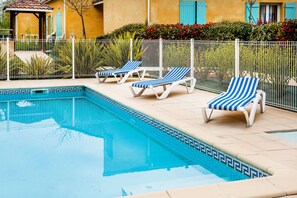 A swimming pool with blue and white striped lounge chairs and a white fence.