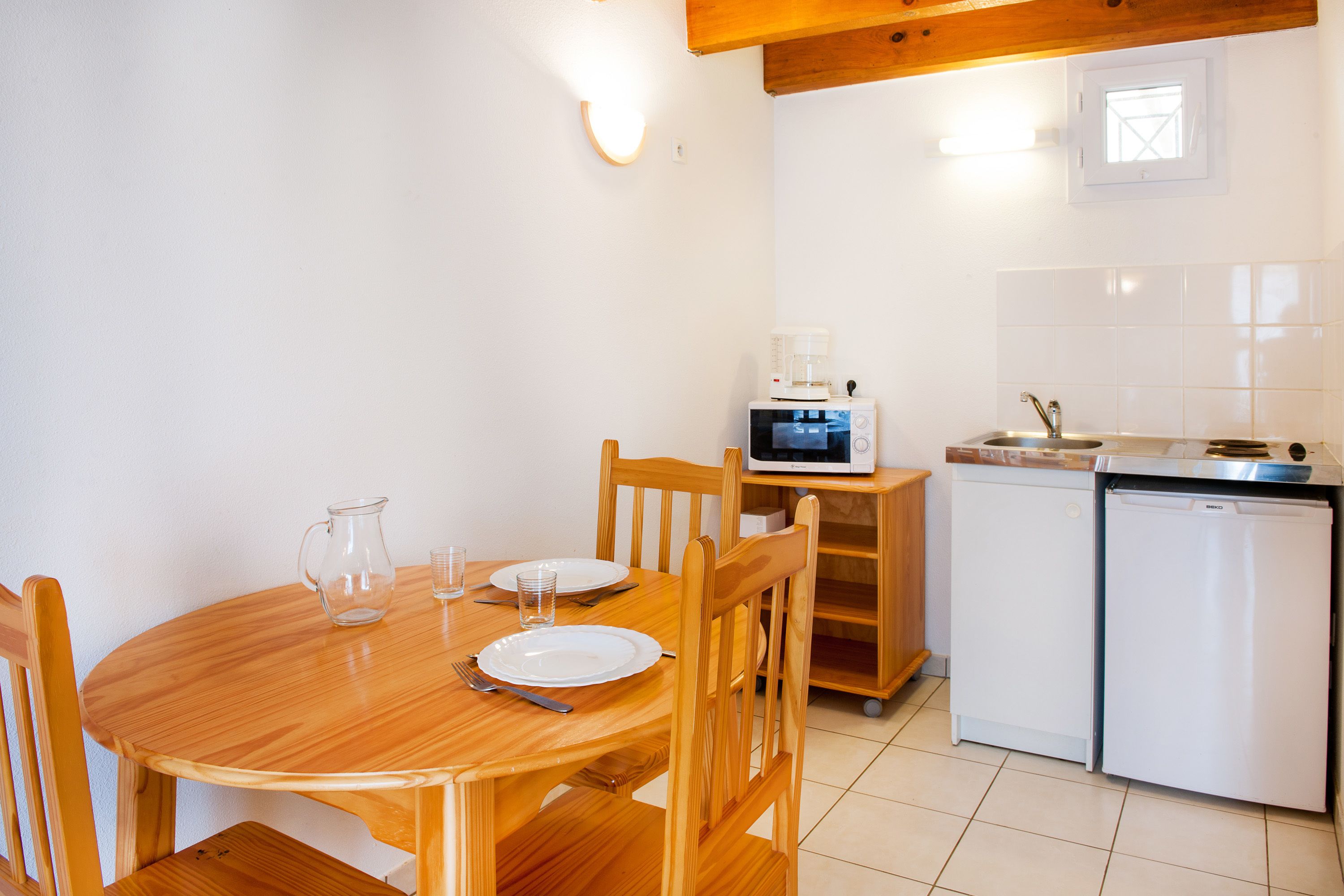 A compact kitchen with a wooden table, chairs, a microwave, a dishwasher, and a small window.