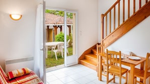 A room with a bed, a dining table with chairs, a staircase, and a sliding glass door leading to an outdoor area. - Résidence Saskia (Cazaubon)