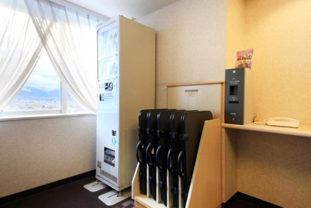 A hotel room with a window, a minibar, a telephone, and a wall-mounted heater.
