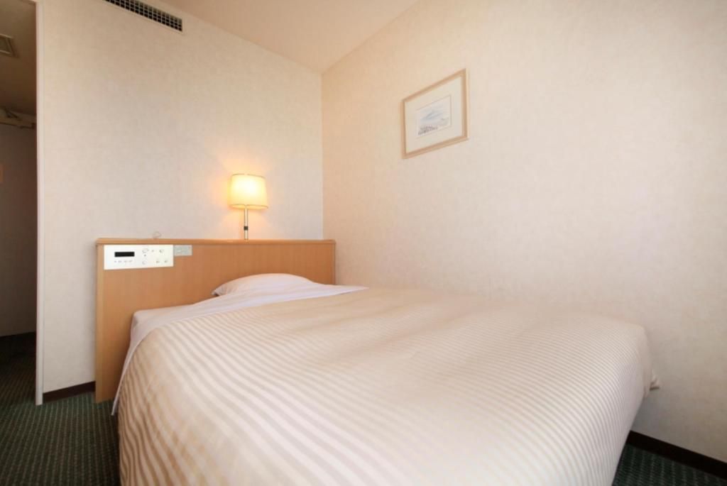 Una habitación de hotel con una cama, una mesita de noche, una lámpara de pared y un cuadro enmarcado.