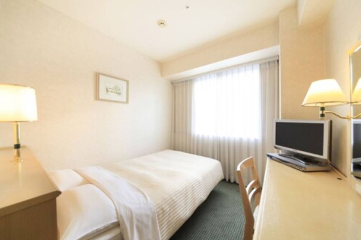 Una habitación de hotel con una cama individual, un escritorio con televisor, una silla y una lámpara.