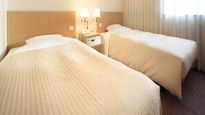 Een hotelkamer met twee bedden, een nachtkastje met lampen en een raam met gordijnen.
