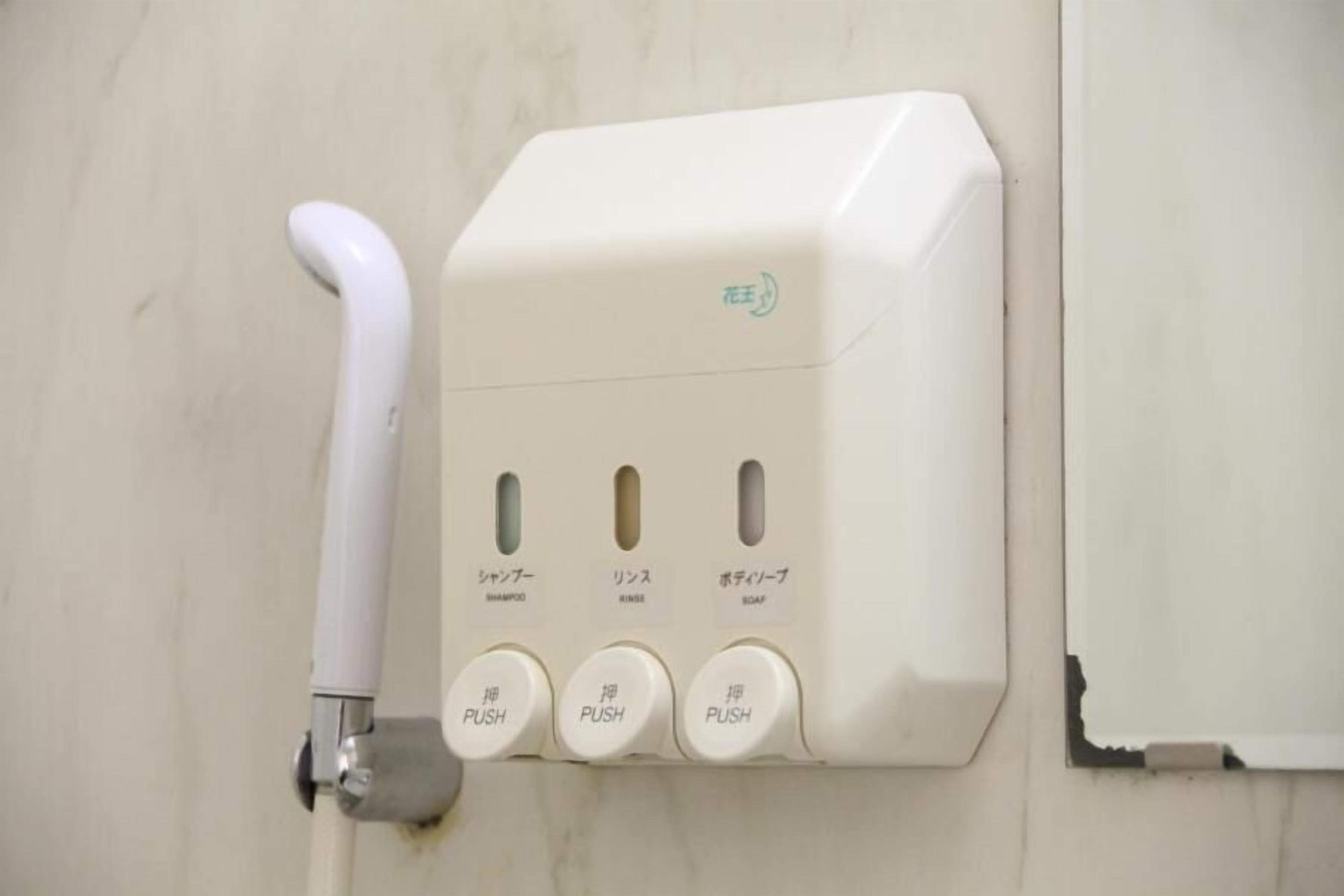 A wall-mounted soap dispenser with three push buttons labeled for shampoo, rinse, and soap.