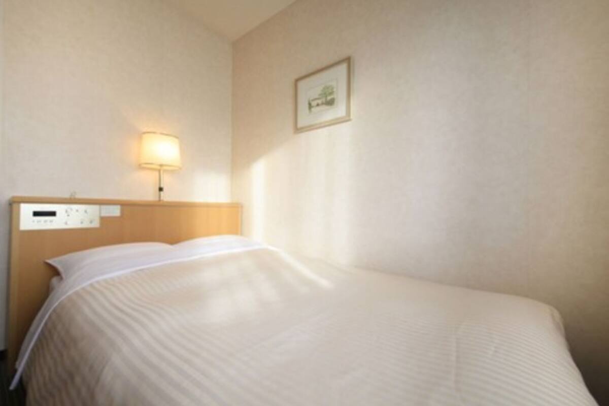 Una habitación de hotel con cama, mesita de noche, lámpara y panel de control en la pared.