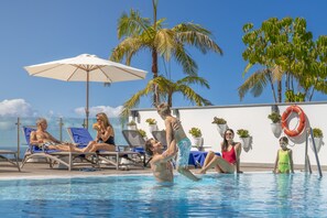 A poolside area with lounge chairs, umbrellas, and palm trees.