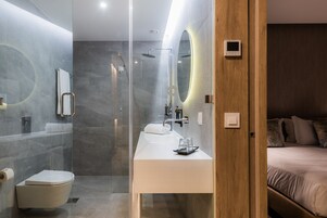A modern bathroom with a glass-enclosed shower, a white sink, and a wooden door leading to a bedroom.