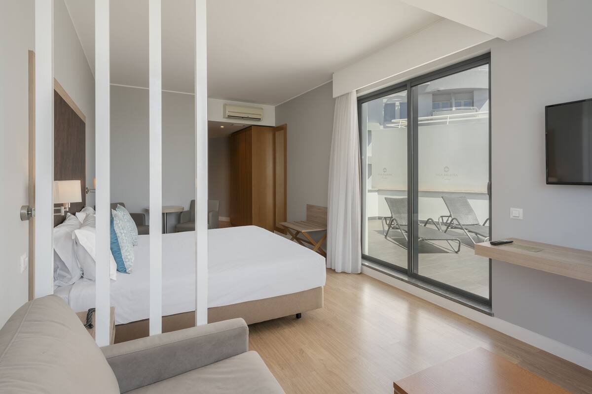 Une chambre d’hôtel moderne dotée d’un grand lit, d’un canapé, d’une télévision et d’un balcon avec des chaises.