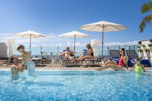 Ein Poolbereich mit Liegestühlen und Sonnenschirmen, ein klarer Himmel und Blick auf das Meer.