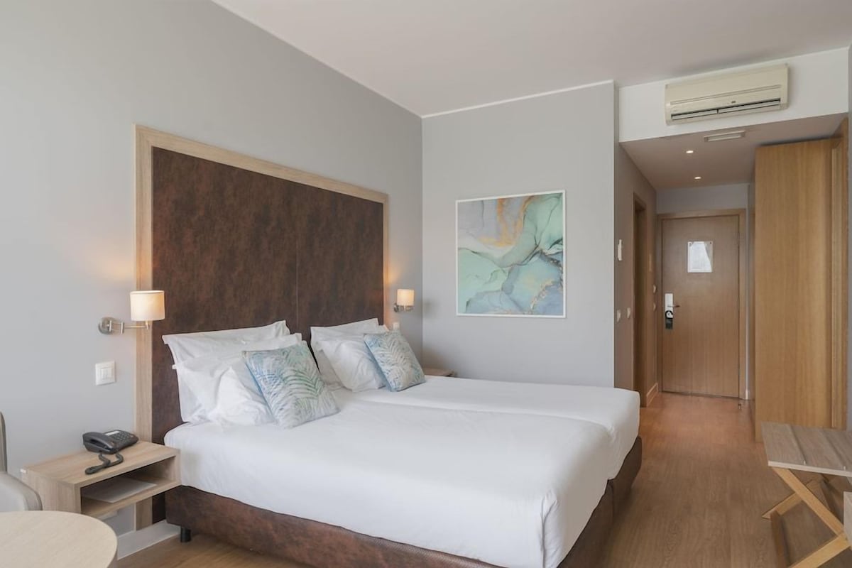A hotel room with a large bed, bedside tables, a desk, and a painting on the wall.