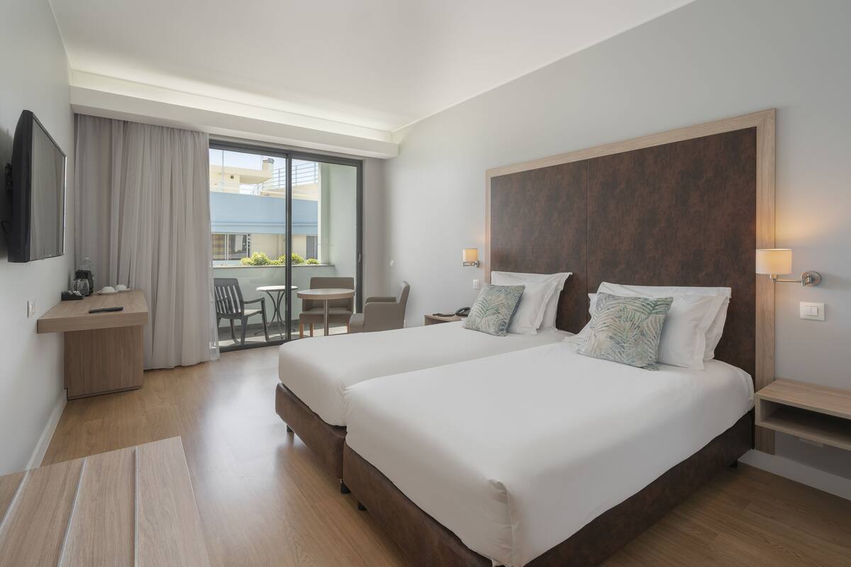 Une chambre d’hôtel avec deux lits, un bureau, une chaise, une télévision et un balcon avec vue.