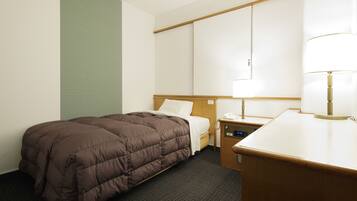 A hotel room with a single bed, a bedside table with a lamp, a small desk, and a wall-mounted TV.