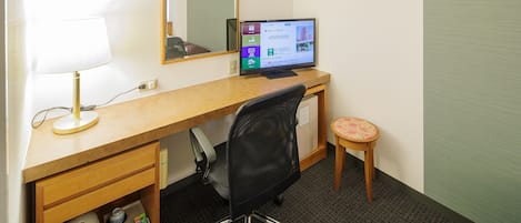 A hotel room with a wooden desk, a computer, a chair, a small stool, and a kettle.