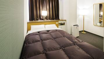 A hotel room with a bed, a bedside lamp, a mirror, and a wall-mounted heater.