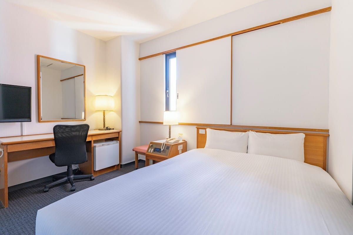 Ein Hotelzimmer mit einem großen Bett, einem Schreibtisch mit Stuhl, einem Fernseher und einer Schreibtischlampe.