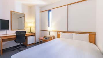 A hotel room with a large bed, a desk with a chair, a television, and a desk lamp.