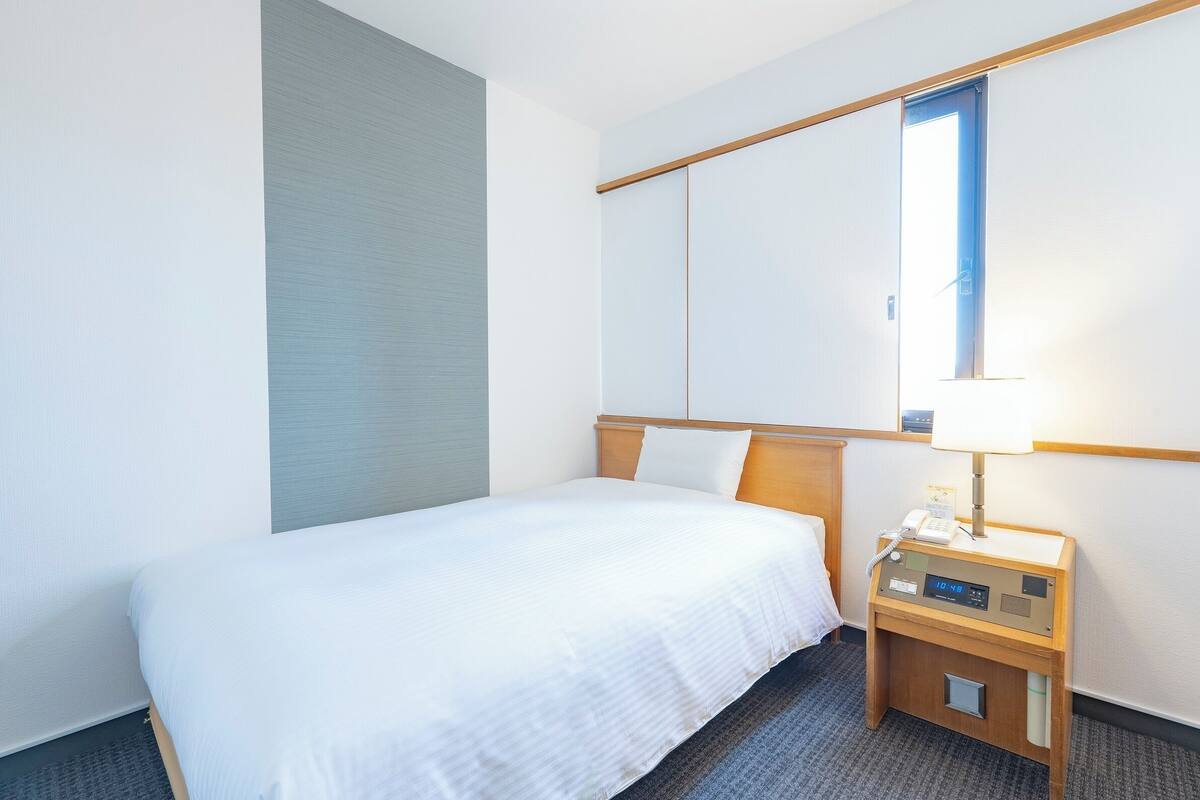 Ein Hotelzimmer mit Bett, Nachttisch mit Lampe und einem großen Spiegel an der Wand.