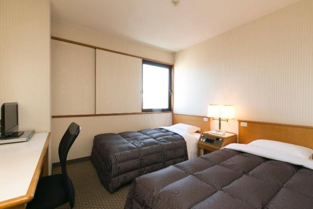 Habitación de hotel con dos camas, un escritorio, una silla, un televisor y una ventana.