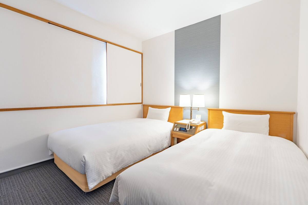 Ein Hotelzimmer mit zwei Betten, einem Nachttisch mit Lampe und einem großen Fenster.