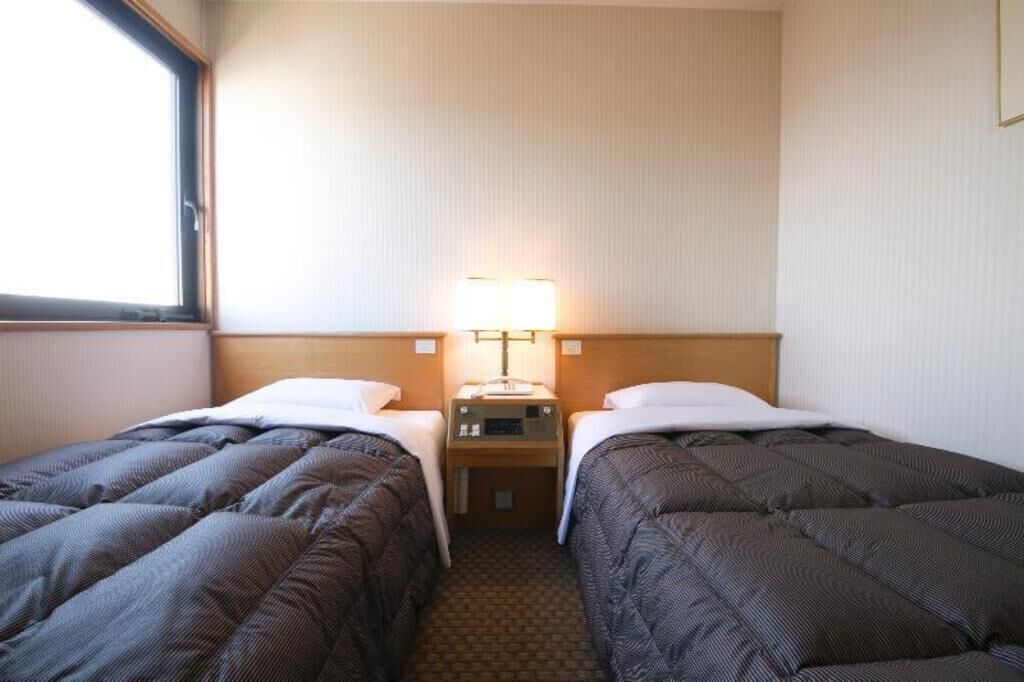 Ein Hotelzimmer mit zwei Betten, einem Nachttisch, einer Lampe und einem Fenster.