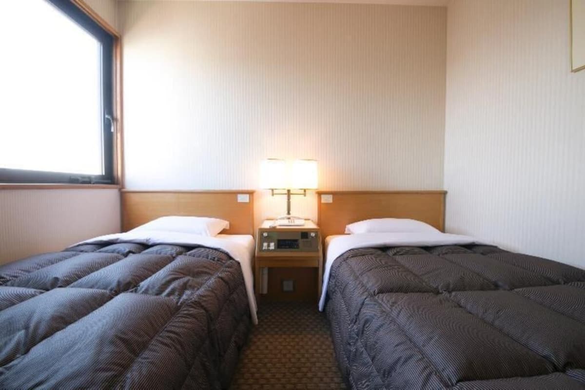 Ein Hotelzimmer mit zwei Betten, einem Nachttisch, einer Lampe und einem Fenster.