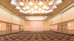 A large conference room with a patterned carpet, a central chandelier, and multiple doors with green exit signs.