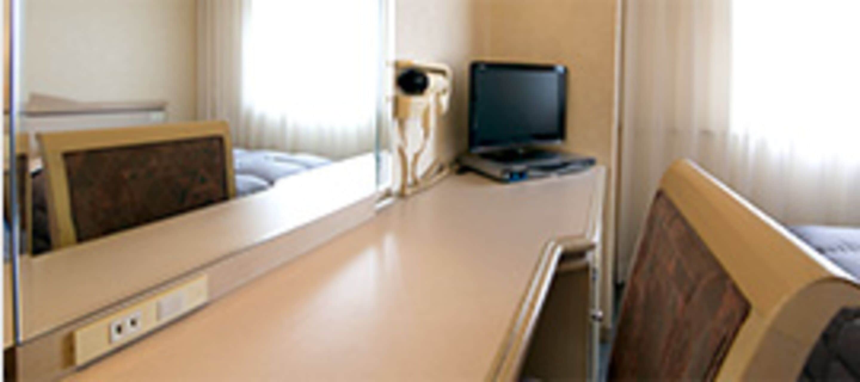 Una habitación de hospital con una cama, una mesita de noche, una silla y un televisor.
