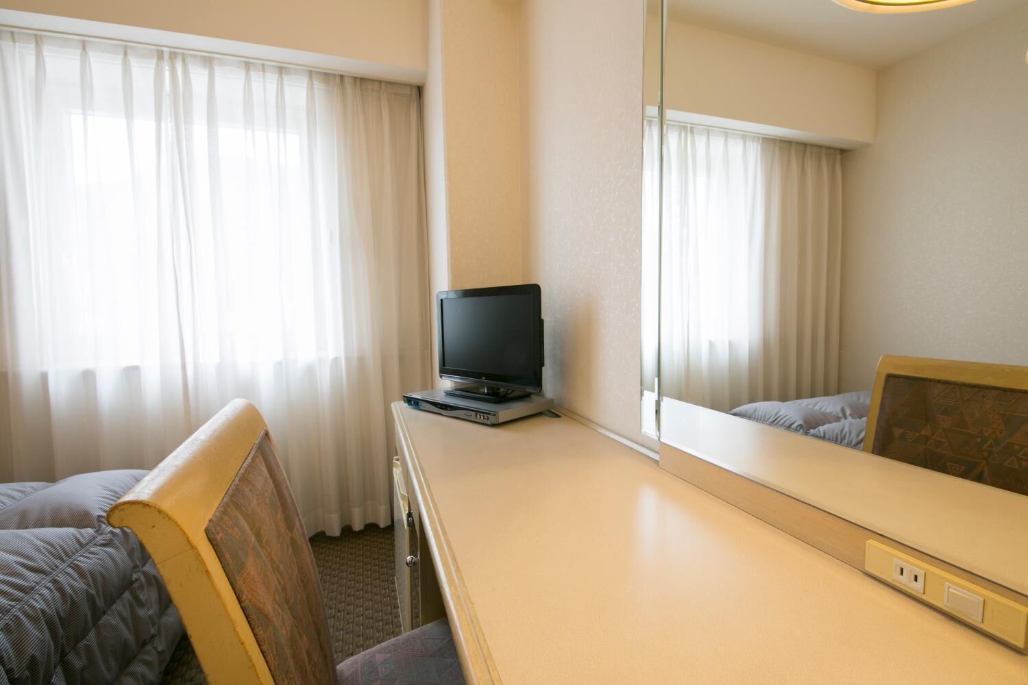 Een hotelkamer met een bed, een bureau met een televisie en een grote spiegel.