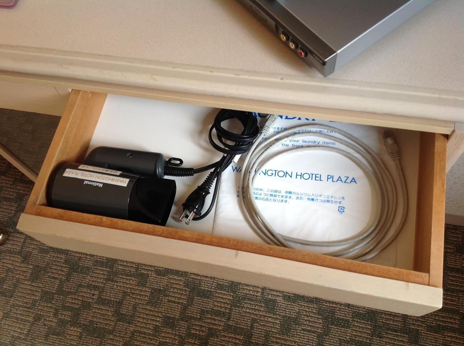 A drawer containing a power adapter, a cable, and a hotel-branded item.
