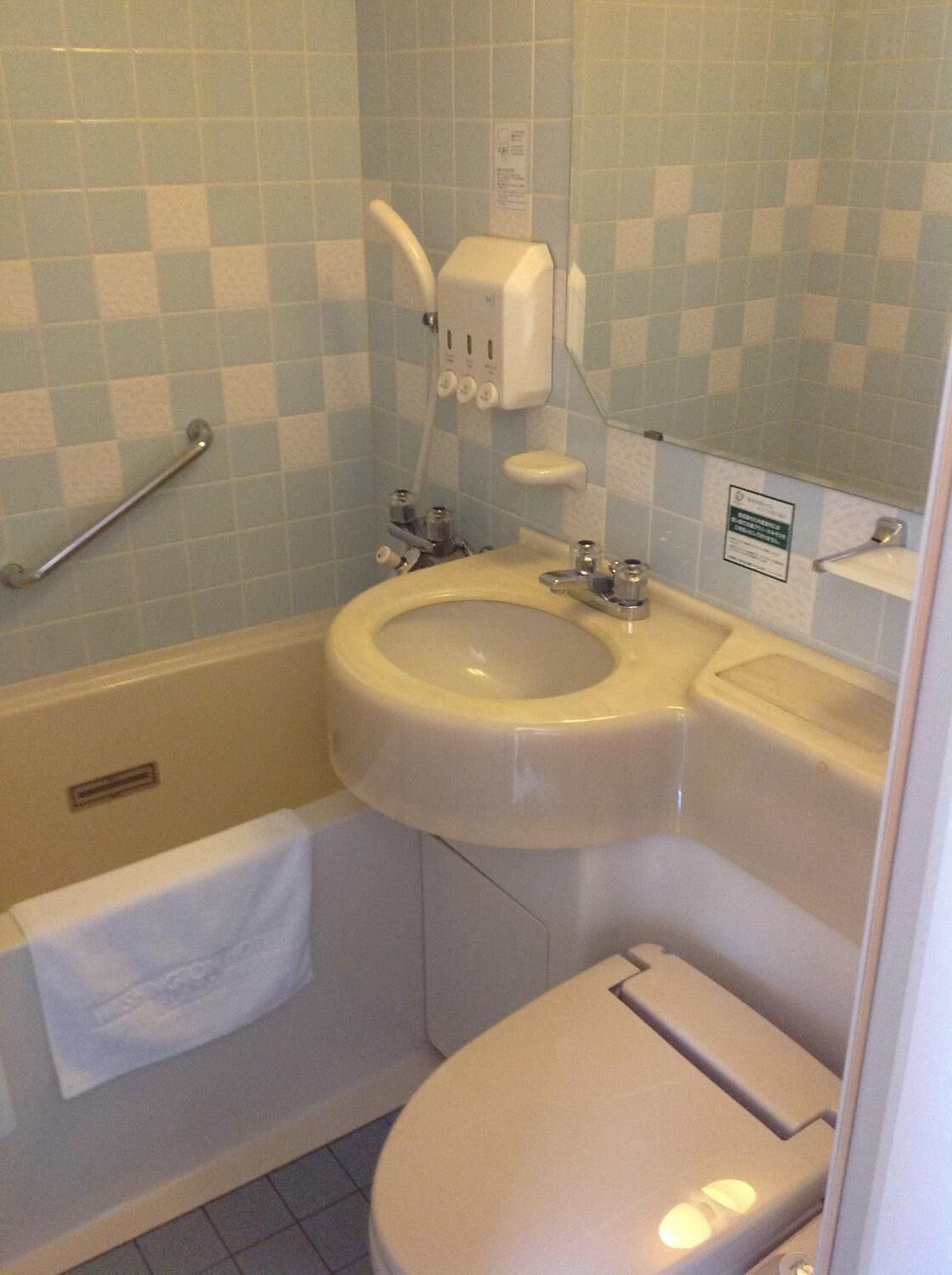A bathroom with a sink, toilet, and bathtub. There is a towel rack and a soap dispenser.