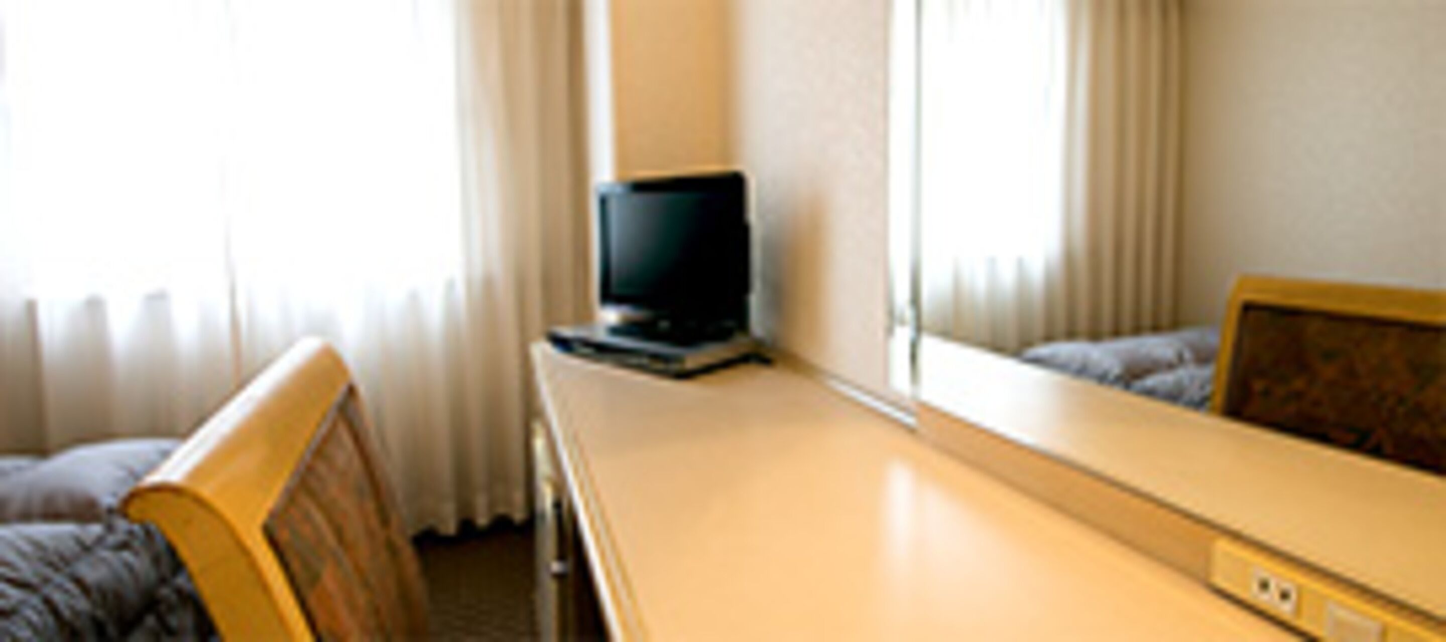 Ein Hotelzimmer mit Bett, Schreibtisch mit Fernseher und Fenster mit Vorhängen.