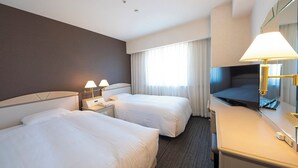 A hotel room with two beds, a desk with a TV, and a window with curtains.