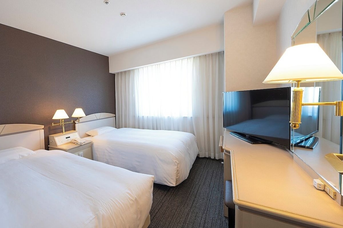 Une chambre d’hôtel avec deux lits, un bureau avec une télévision et une fenêtre avec des rideaux.