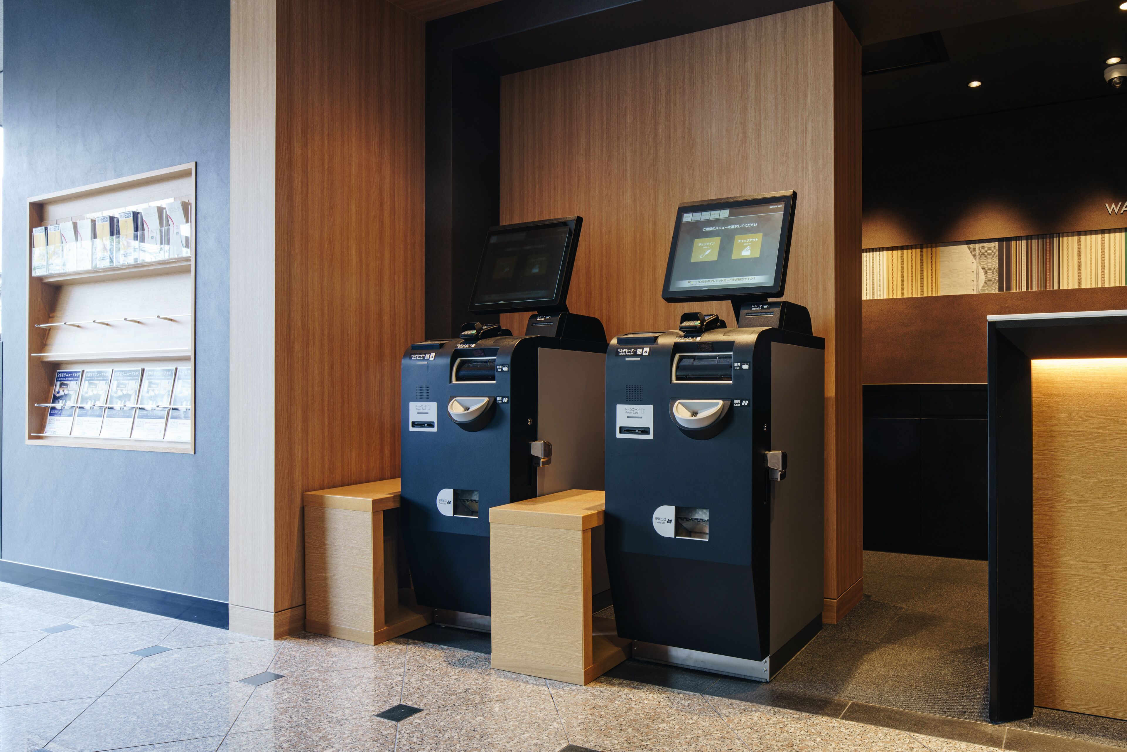 A self-service kiosk area with two machines, a wooden counter, and a shelf with brochures.
