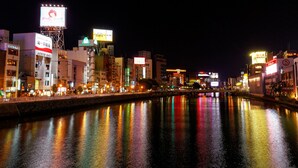 A nighttime cityscape with illuminated buildings and a river reflecting lights.