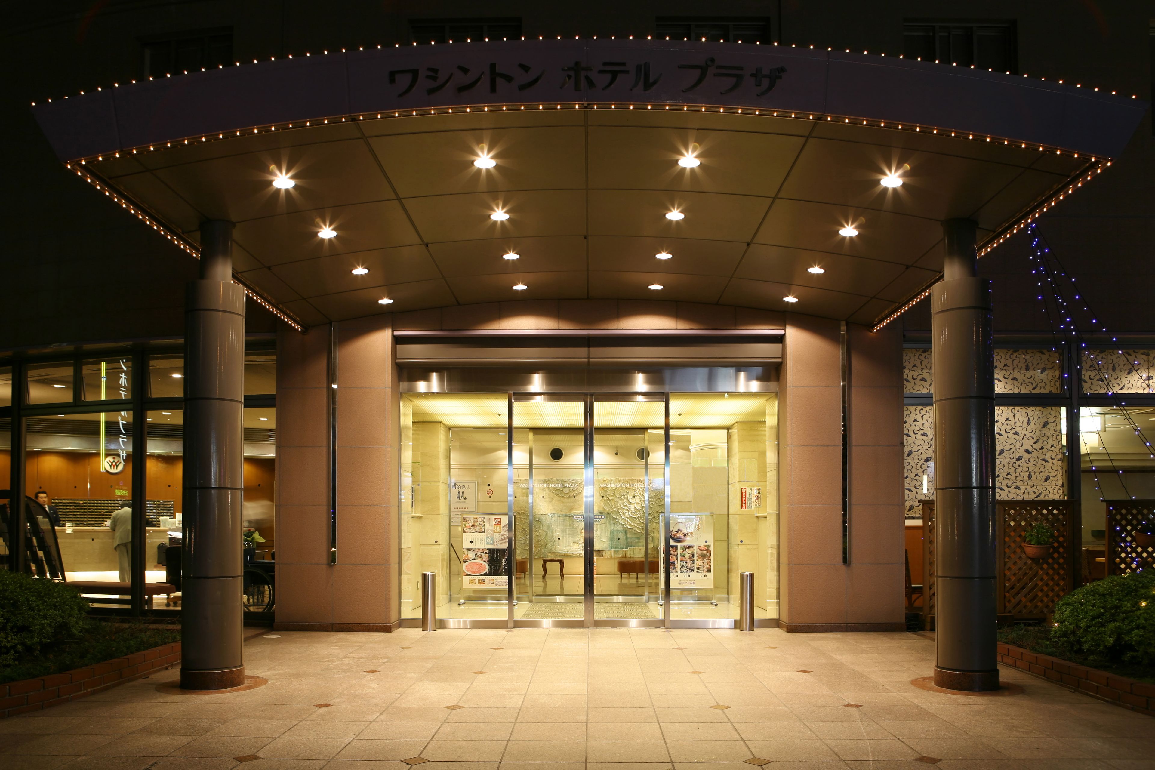 L’entrée d’un hôtel, avec une porte en verre, un espace d’attente abrité et une enseigne au-dessus de l’entrée.