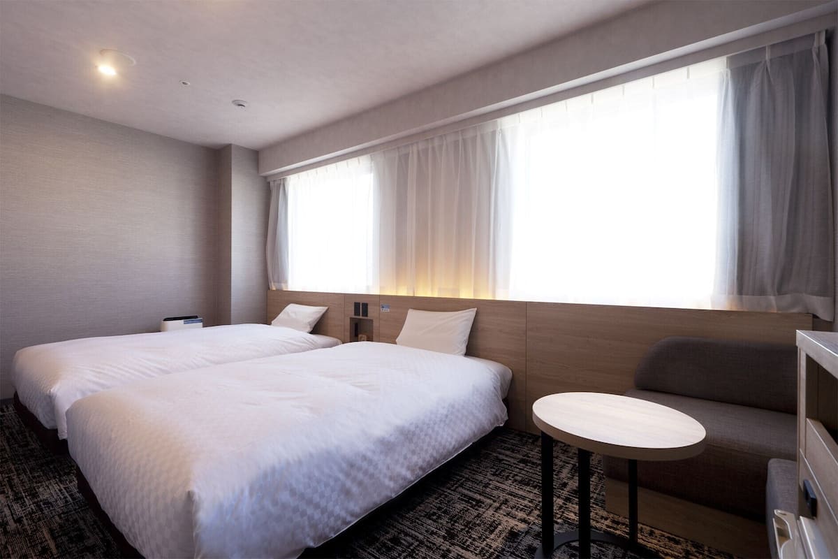 Ein Hotelzimmer mit zwei Betten, einem kleinen runden Tisch und einem Sofa.