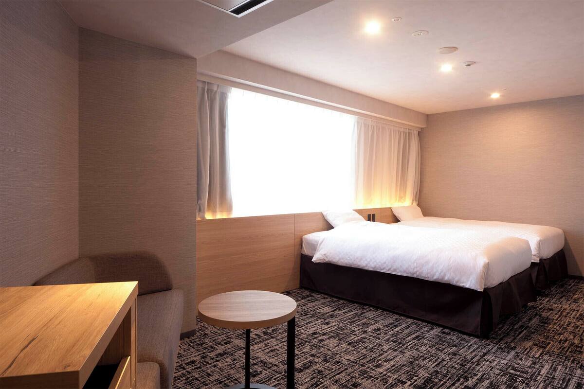 Ein Hotelzimmer mit Bett, rundem Tisch und einem fenster mit Vorhängen.